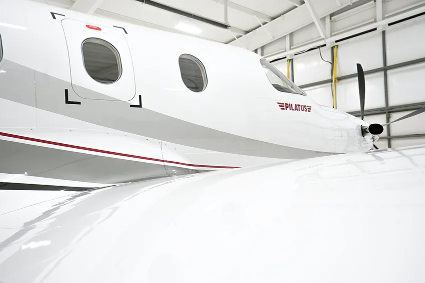 A close-up view of the front fuselage and wing of a white Pilatus PC-12 aircraft, showing the "PILATUS" logo.