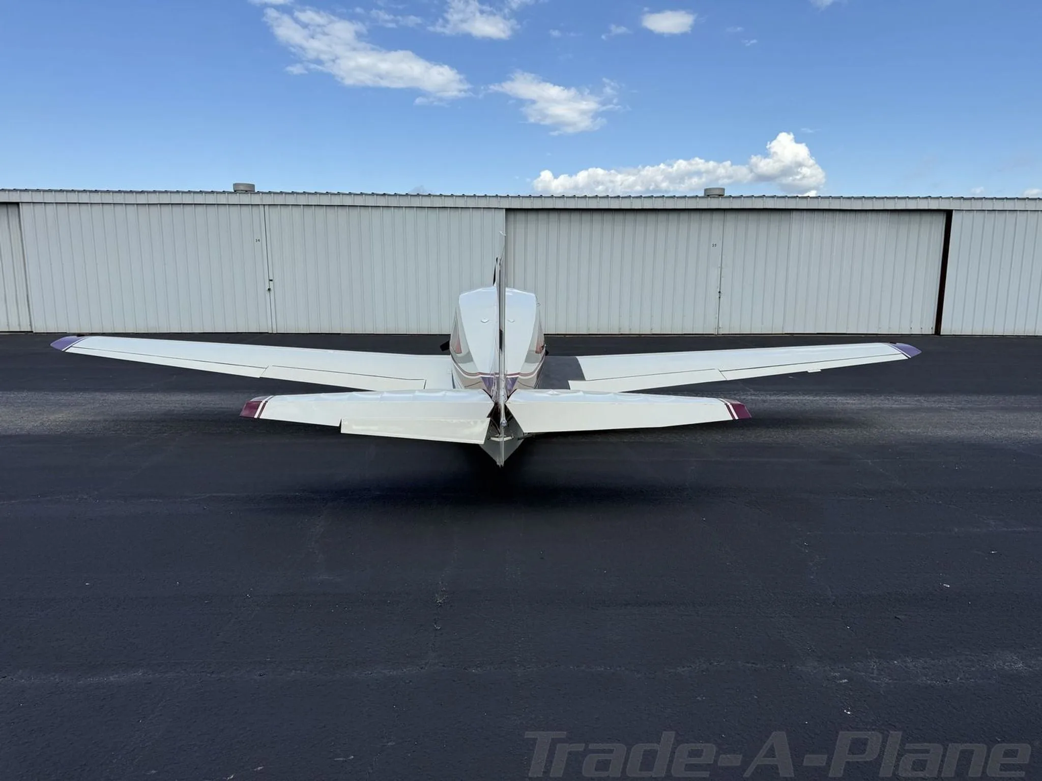 Rear view of a white and maroon Bellanca Viking N63083 parked on a tarmac.