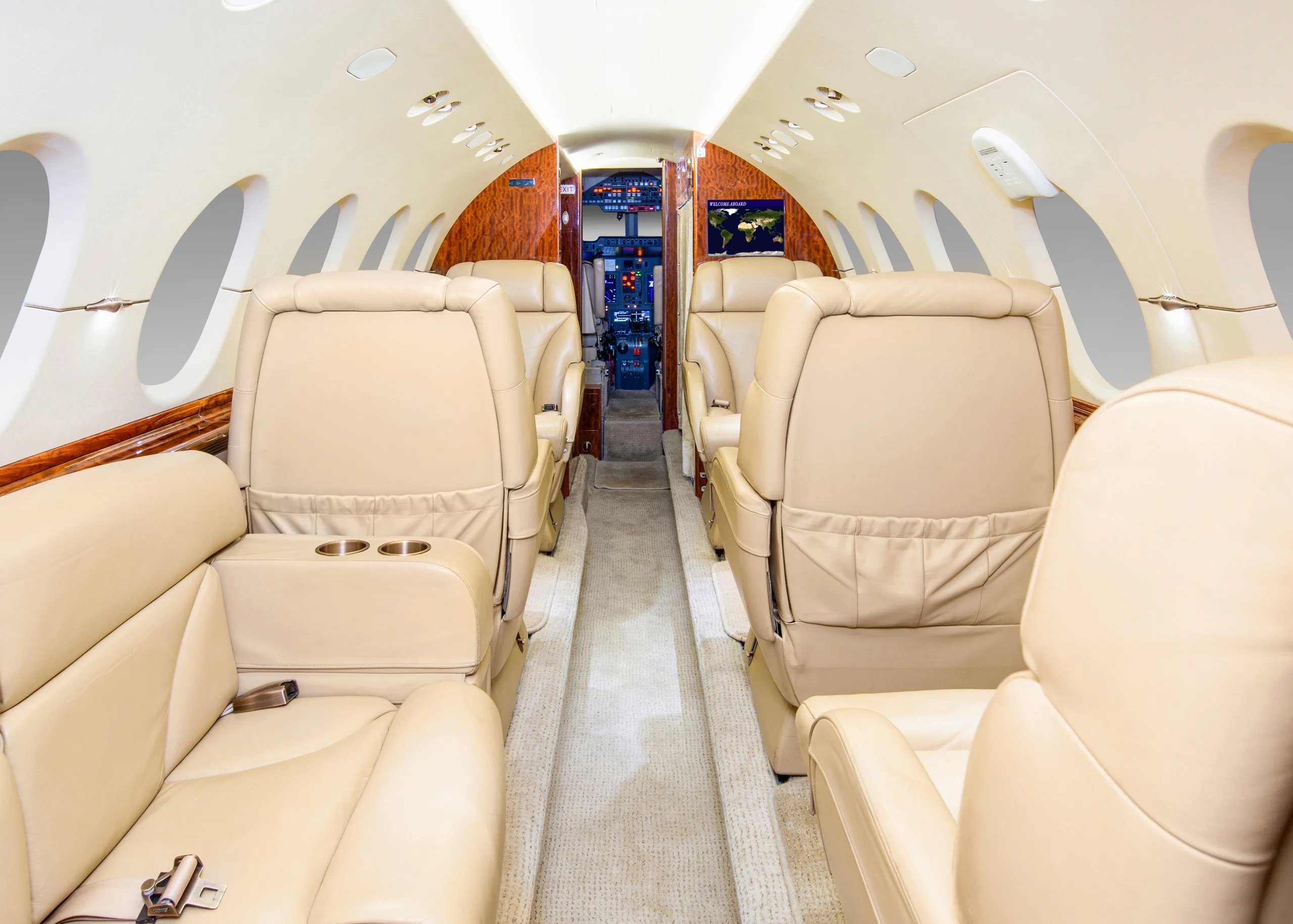 The interior cabin of a private jet, showing rows of beige leather seats and a view towards the rear galley area.