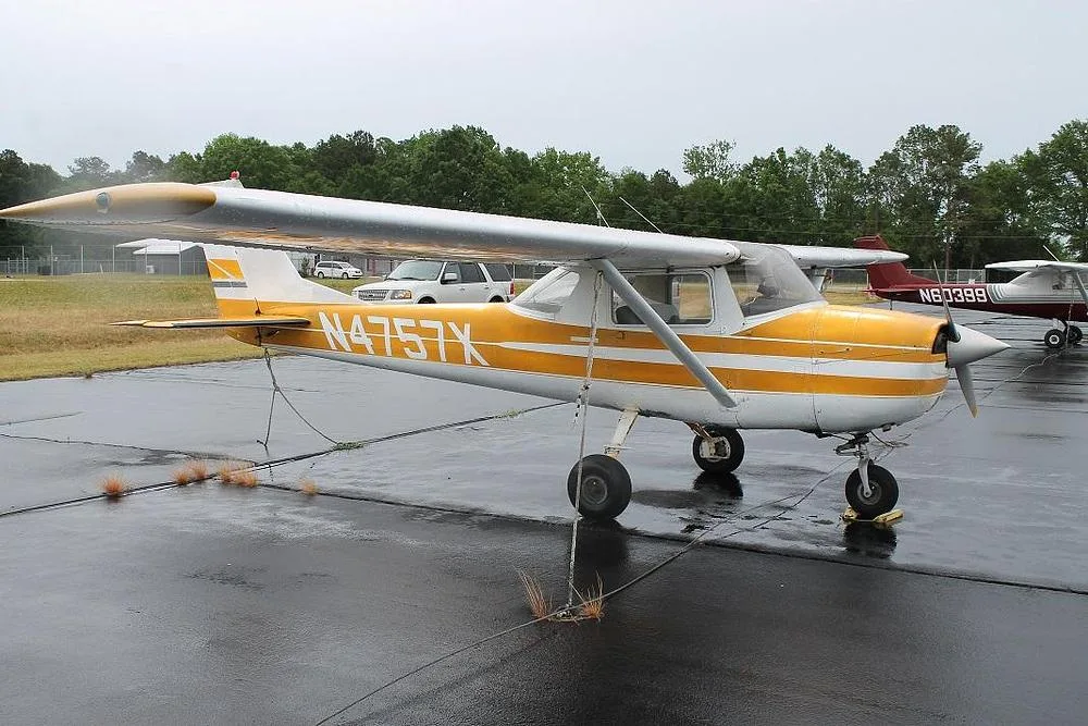 A front-side view of a yellow and white Cessna 150 (or similar) with registration N4757X parked on a wet tarmac.