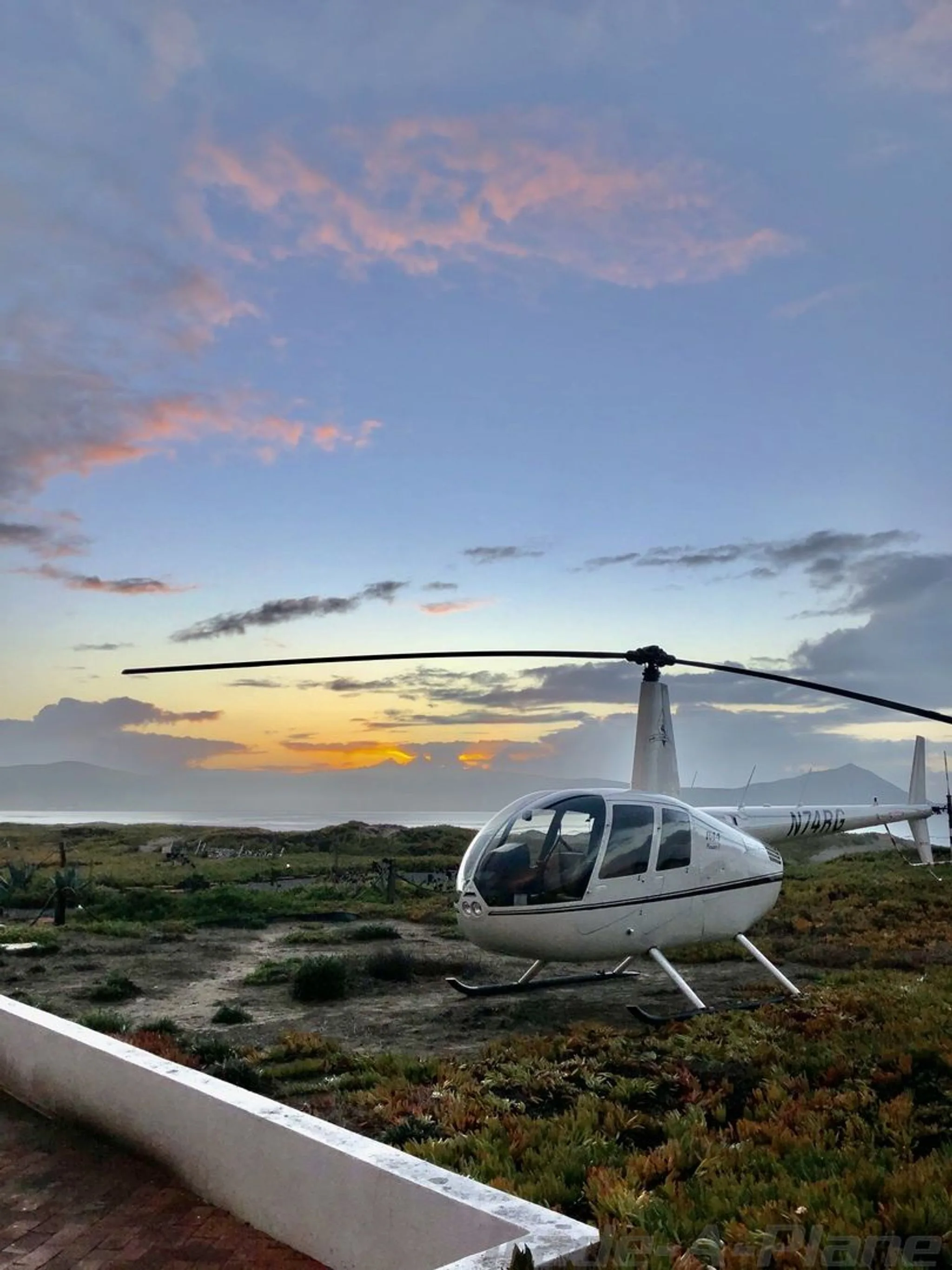 A Robinson R44 Raven I parked on the ground during sunset.