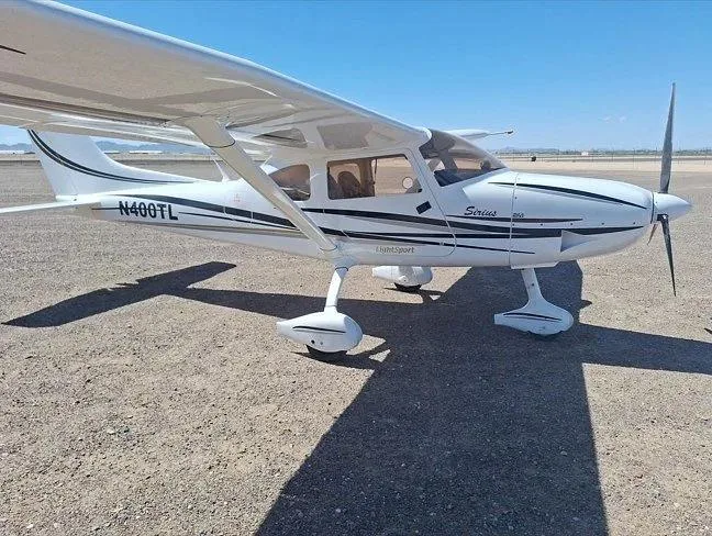 A side view of a white Sirius LightSport aircraft with black and grey stripes, registration N400TL, parked on a gravel surface.