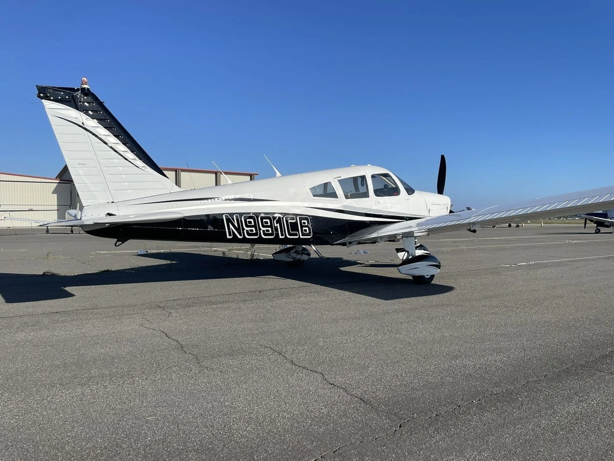 A side view of the white and black Piper Cherokee 235 C aircraft N991CB parked on an airfield.