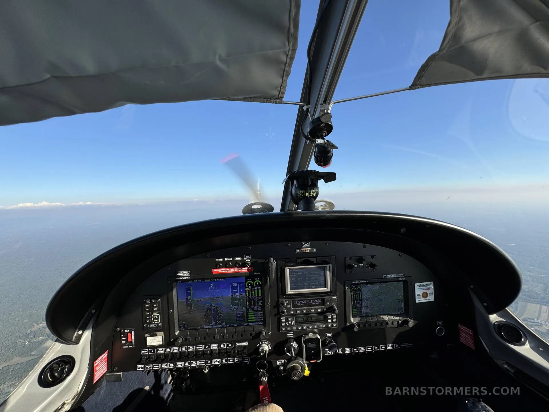 The cockpit of an aircraft in flight, showing the instrument panel with multiple screens and a view of the horizon.