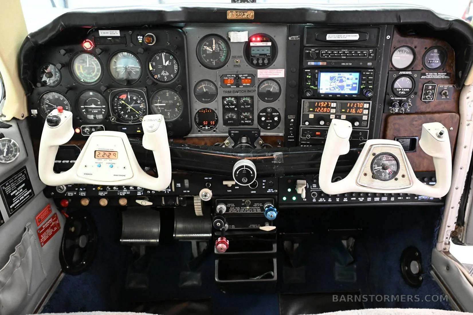The detailed instrument panel and controls of a small aircraft, featuring multiple gauges and two white yokes.