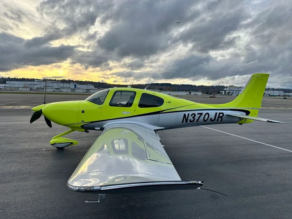 A bright yellow and silver Cirrus SR22 aircraft with registration N370JR parked on an airport tarmac at sunset.