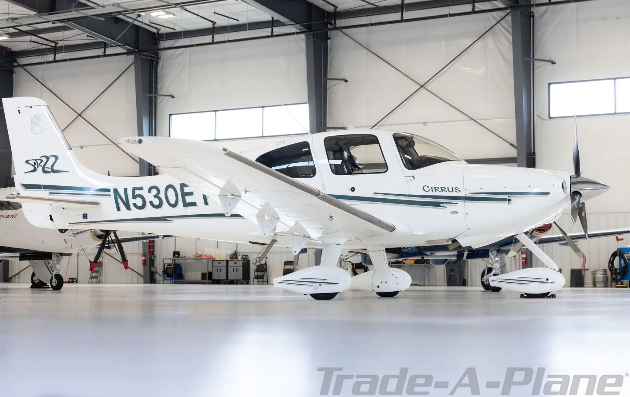 A white Cirrus SR22 aircraft with N530ET registration and green stripes is parked in a hangar, viewed from the front right.