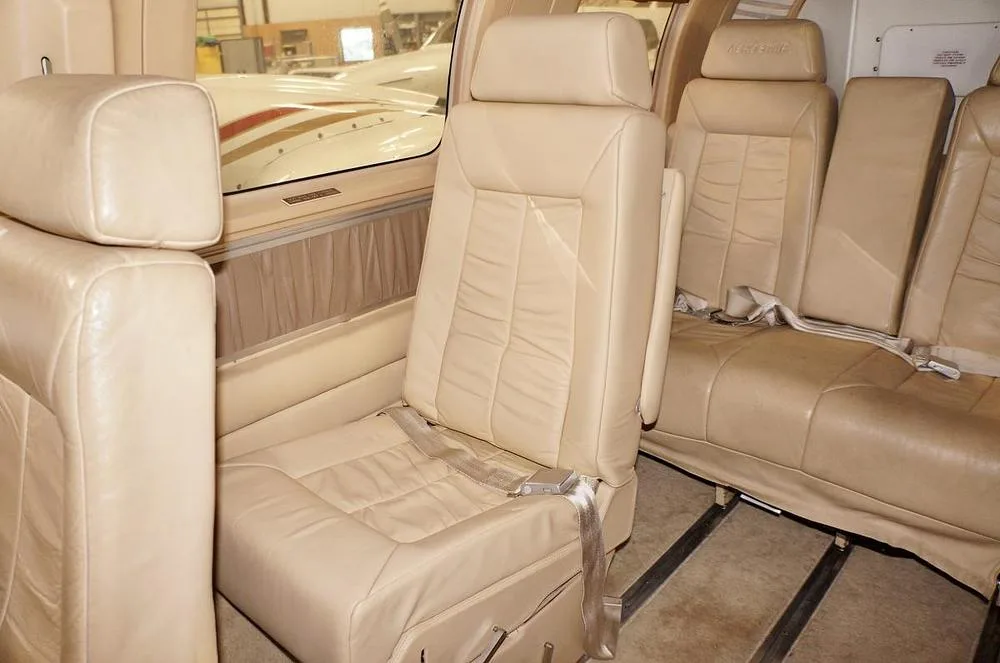 The beige leather interior cabin of a twin-engine aircraft, showing multiple passenger seats with seatbelts.