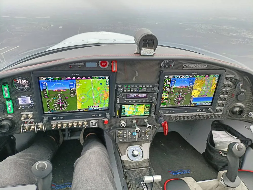 The cockpit of a Bristell aircraft with two large Garmin G3X Touch displays and a pilot's legs visible.