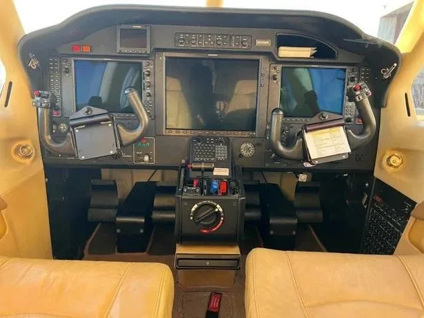 The cockpit of an aircraft features a modern glass panel with multiple displays and tan leather seats.