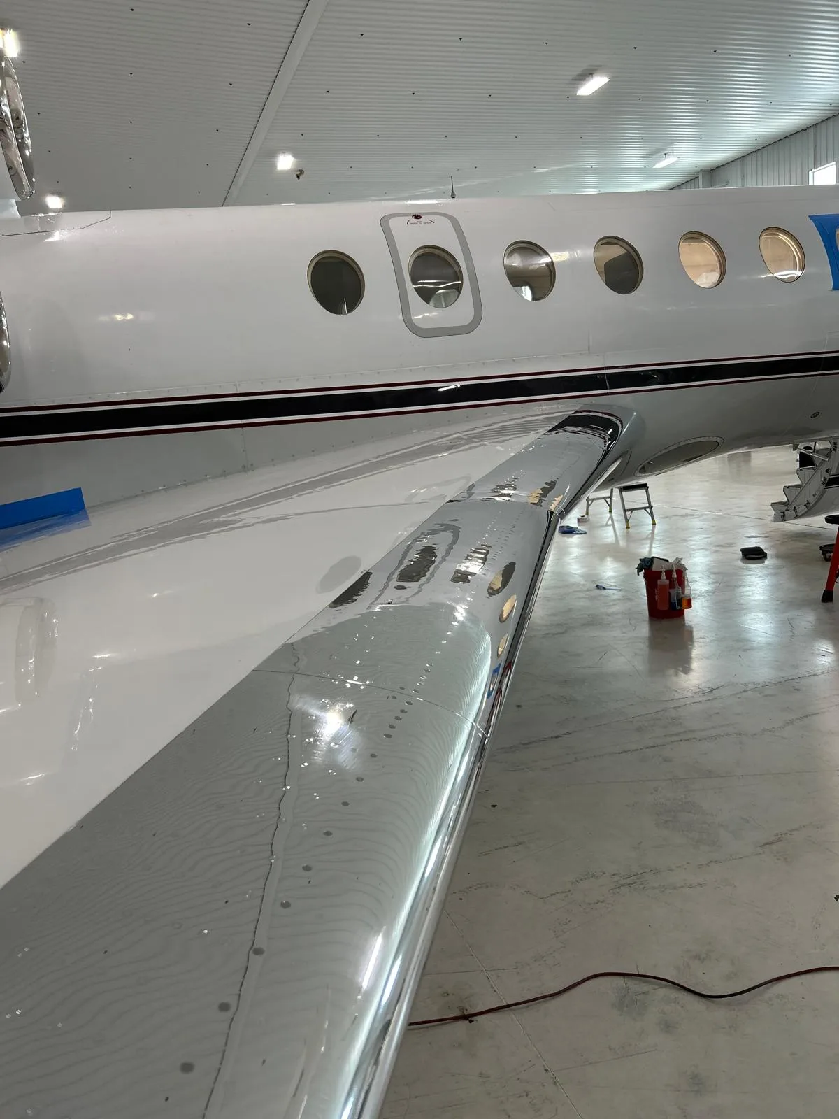 A close-up view of the polished wing and fuselage of a white aircraft inside a hangar.