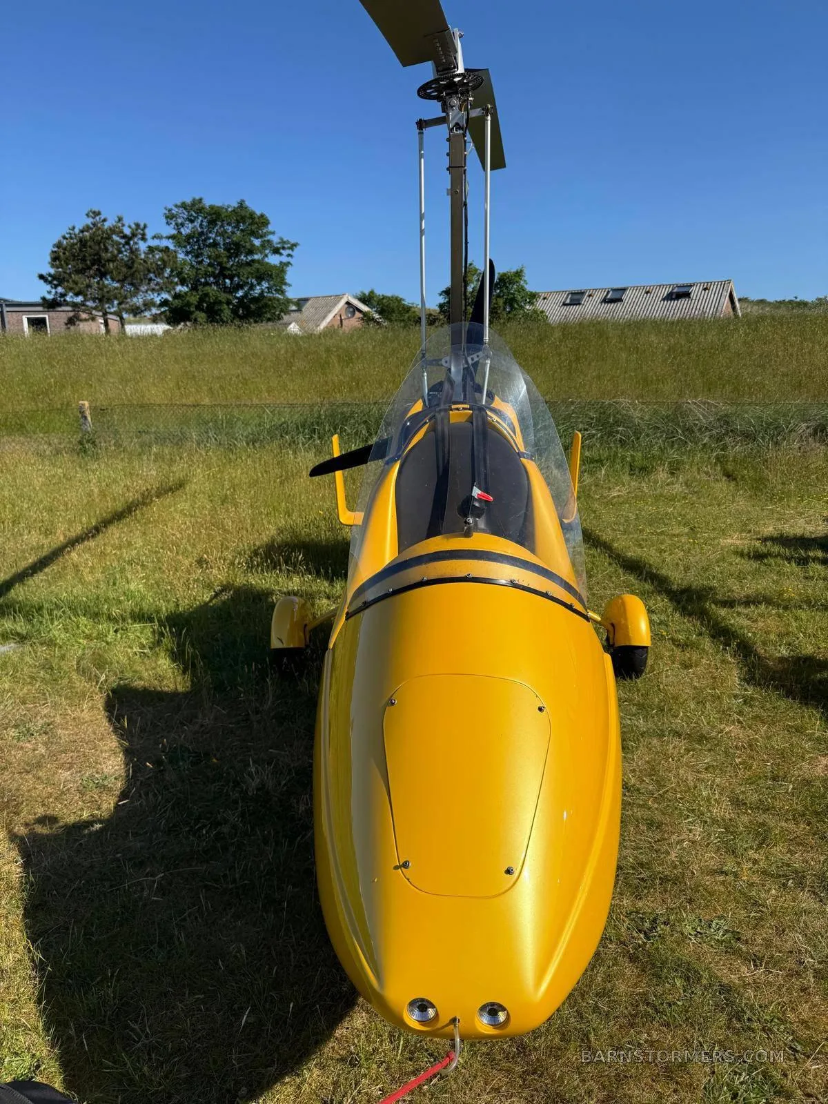 A head-on view of a yellow MTO Sport autogyro parked on a grassy field under a clear blue sky.