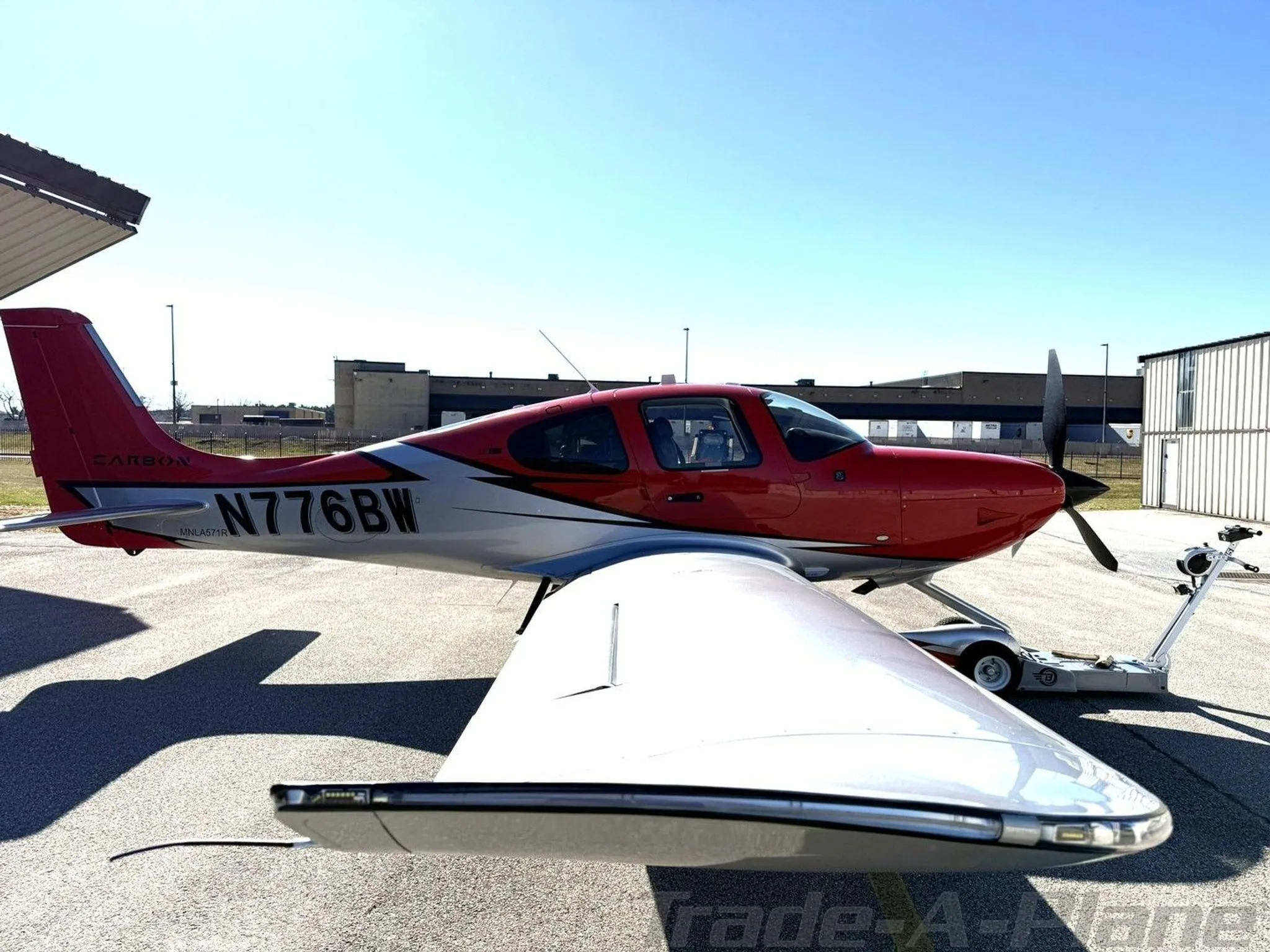 A side view of the red and silver Cirrus SR22T aircraft, N776BW, parked on the tarmac.