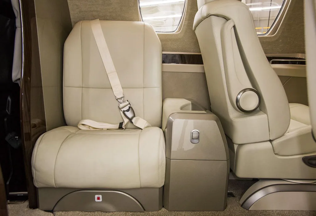 A close-up of a beige leather passenger seat with a seatbelt in the private jet's cabin.