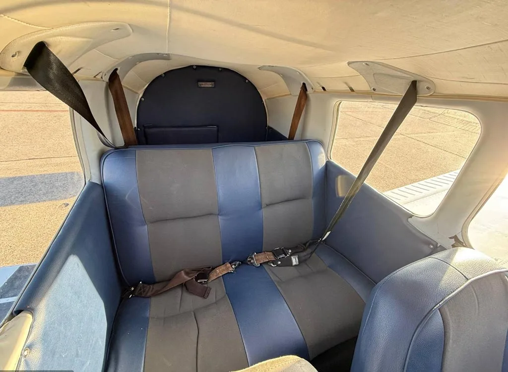 The rear cabin seats of a small aircraft, upholstered in blue and grey fabric with seatbelts.
