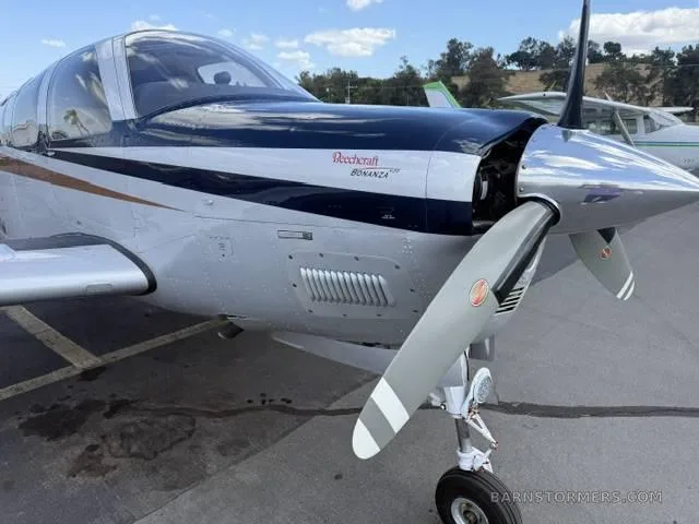 A close-up view of the nose and propeller of a white, blue, and copper Beechcraft Bonanza N926LC.