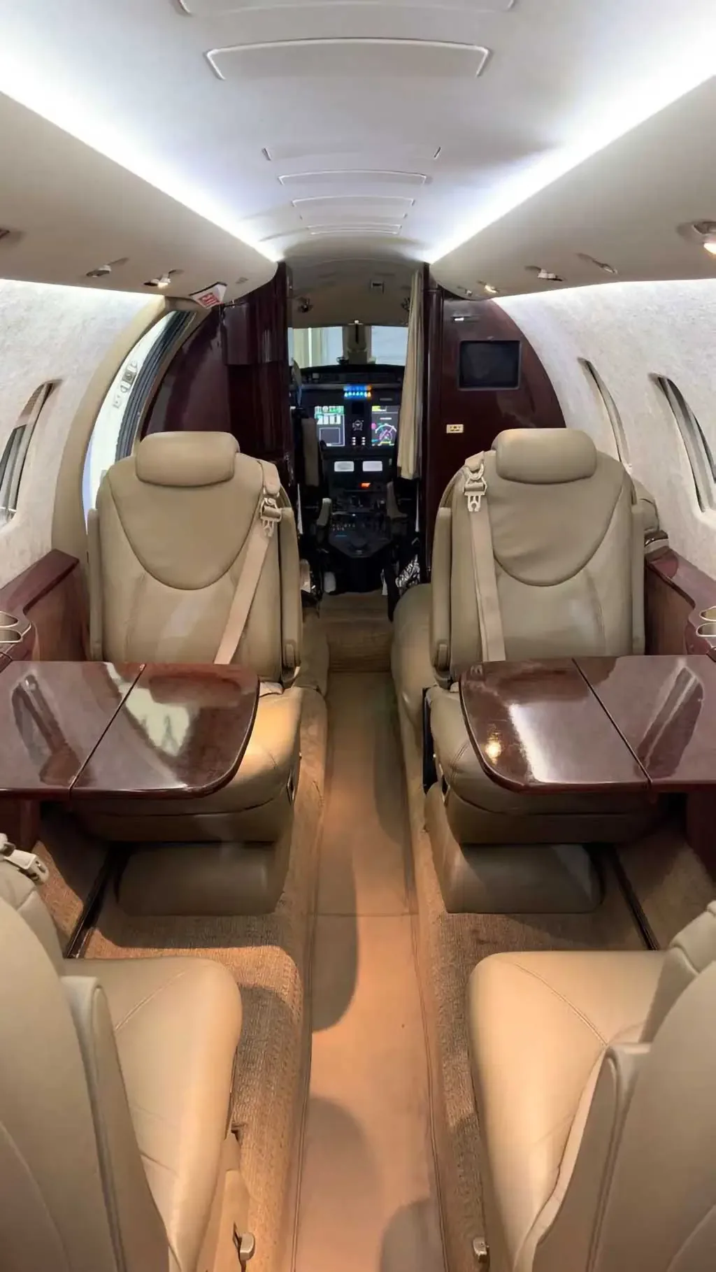 A slightly wider view of the aircraft cabin interior with beige leather seats and folded wooden tables, facing the cockpit.