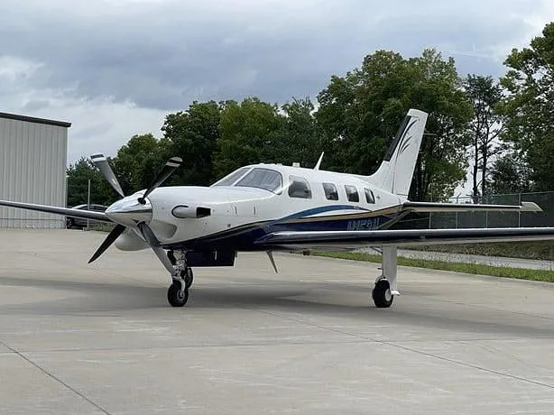 A white and blue single-engine turboprop aircraft, registration N152AL, is parked on a tarmac next to a hangar.