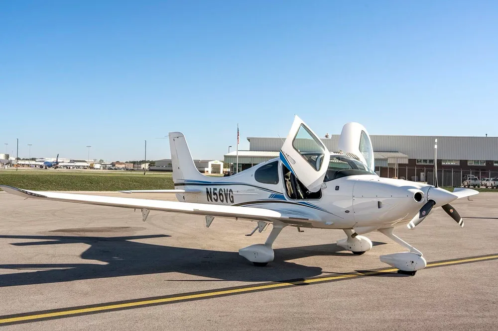 A white Cirrus SR22 aircraft with blue and black stripes, tail number N56VG, parked on an airfield with the pilot's door open.