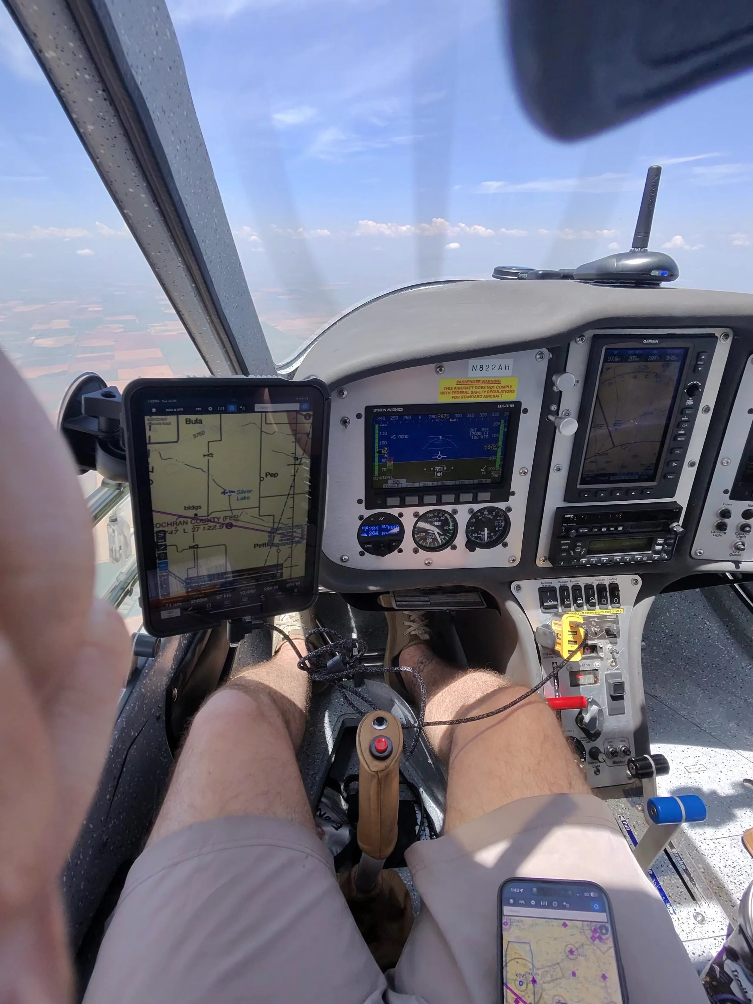A pilot's view from the cockpit of a Flight Design CTLS aircraft in flight, showing the instrument panel, a mounted tablet, and the pilot's legs.