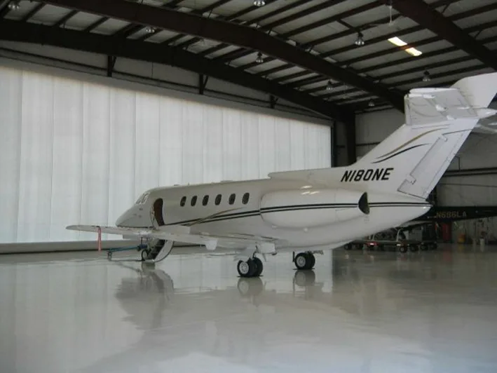 A white business jet with black and gold stripes, tail number N180NE, parked inside a large, brightly lit hangar.