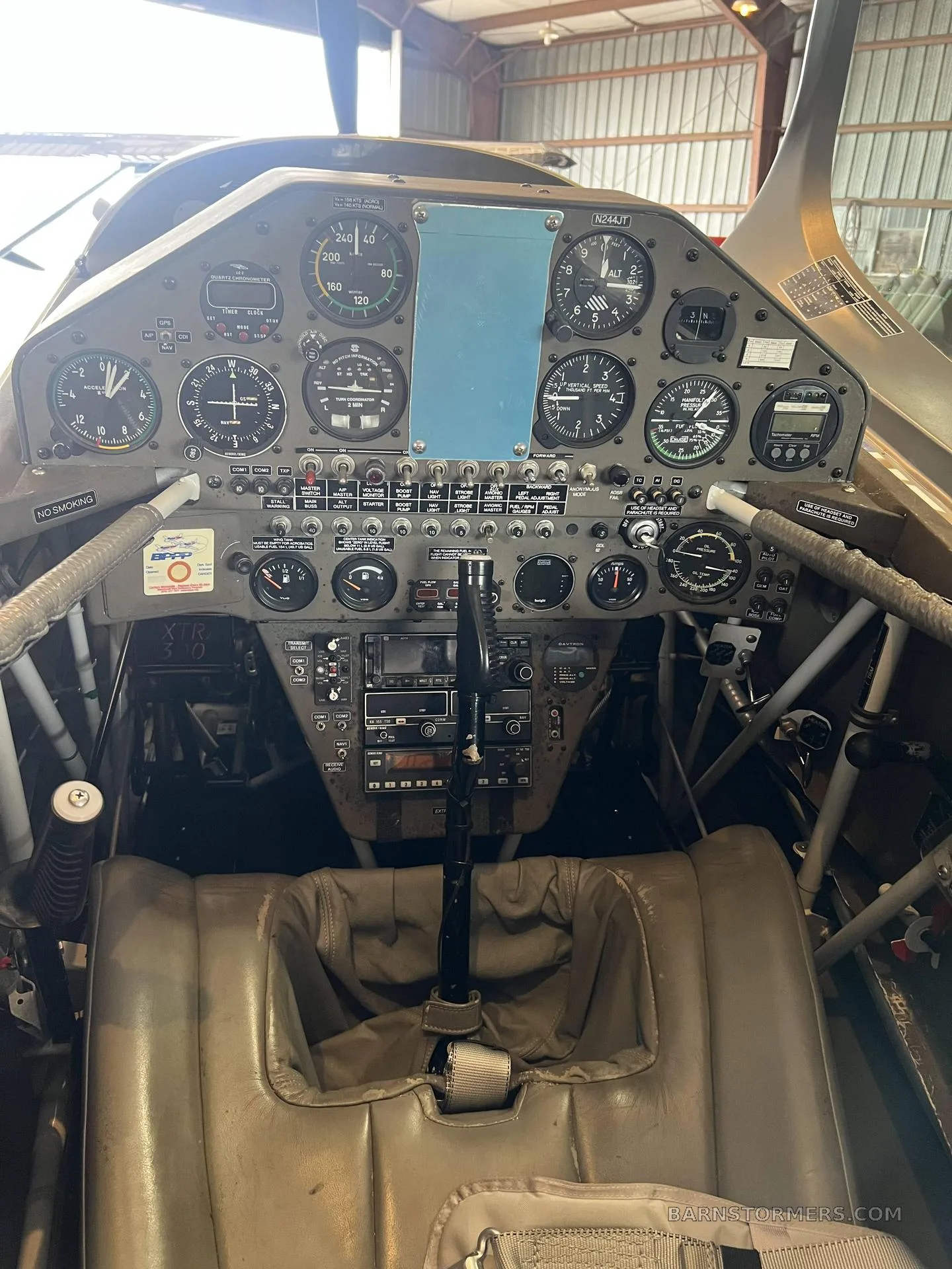 The cockpit of an Extra 300L aircraft, showing the instrument panel, controls, and a tan seat.