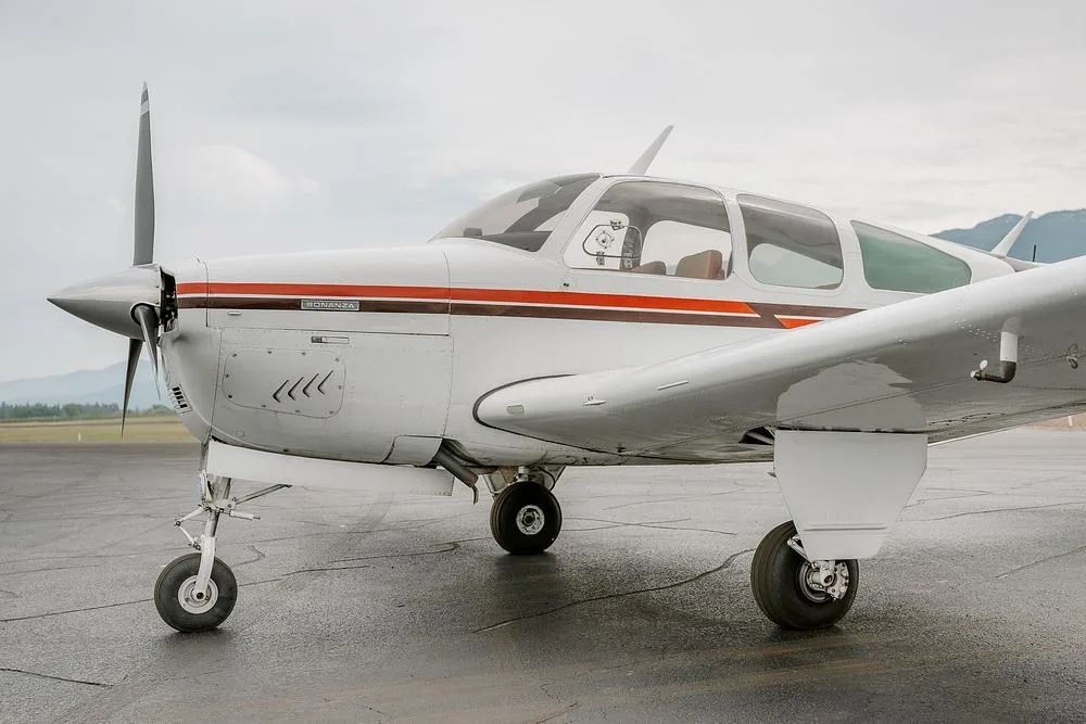 A close-up view of the front right side of a white Beechcraft Bonanza aircraft with brown and orange stripes on a tarmac.