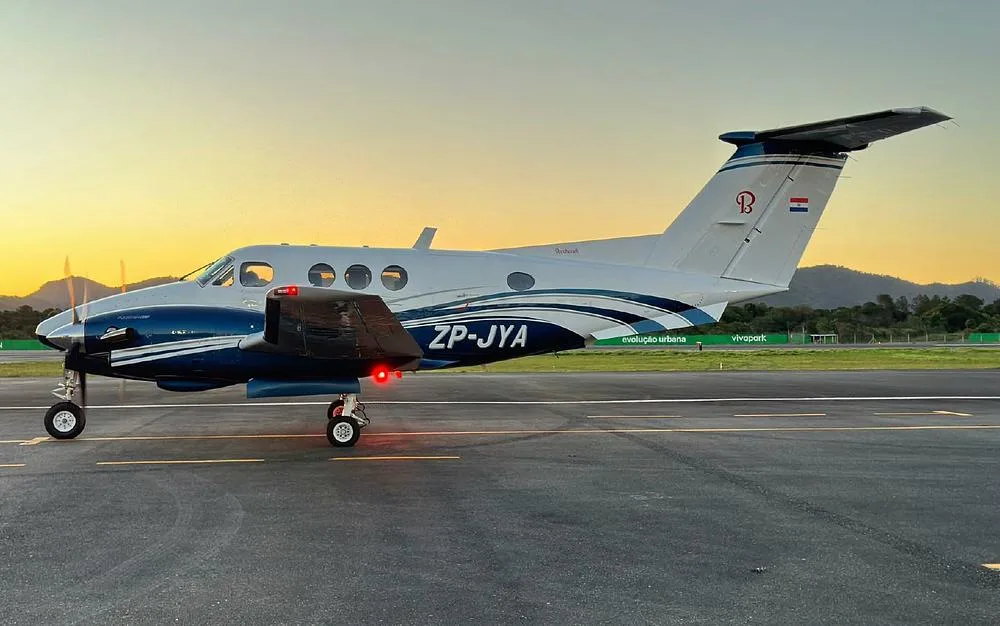 A Beechcraft King Air with blue and white livery, registration ZP-JYA, parked on a tarmac at sunset.