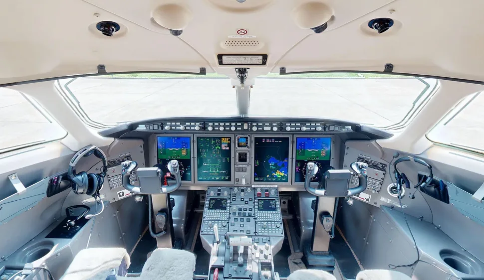 The modern cockpit of a private jet with multiple digital displays and control yokes.