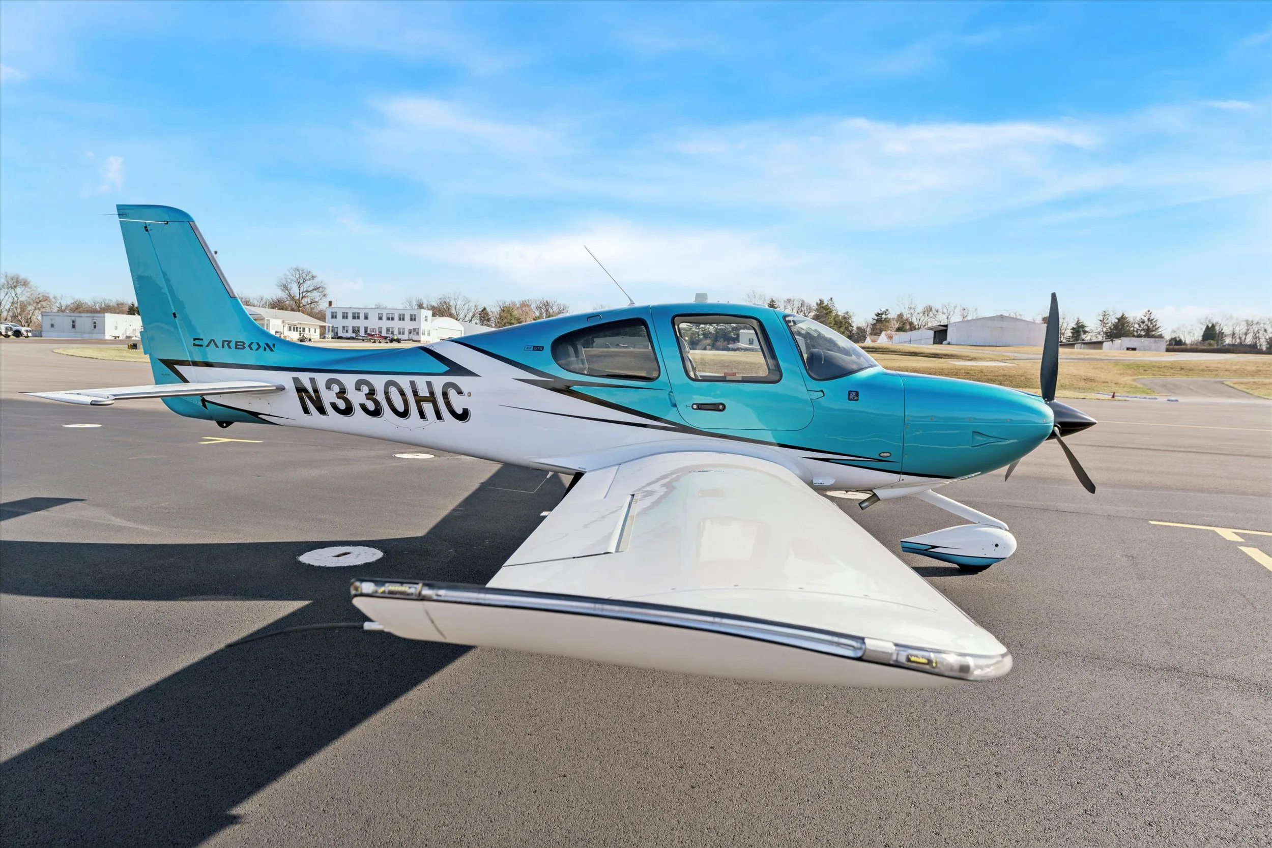A side view of a teal and white Cirrus SR22 aircraft, registration N330HC, parked on an asphalt runway under a clear blue sky.