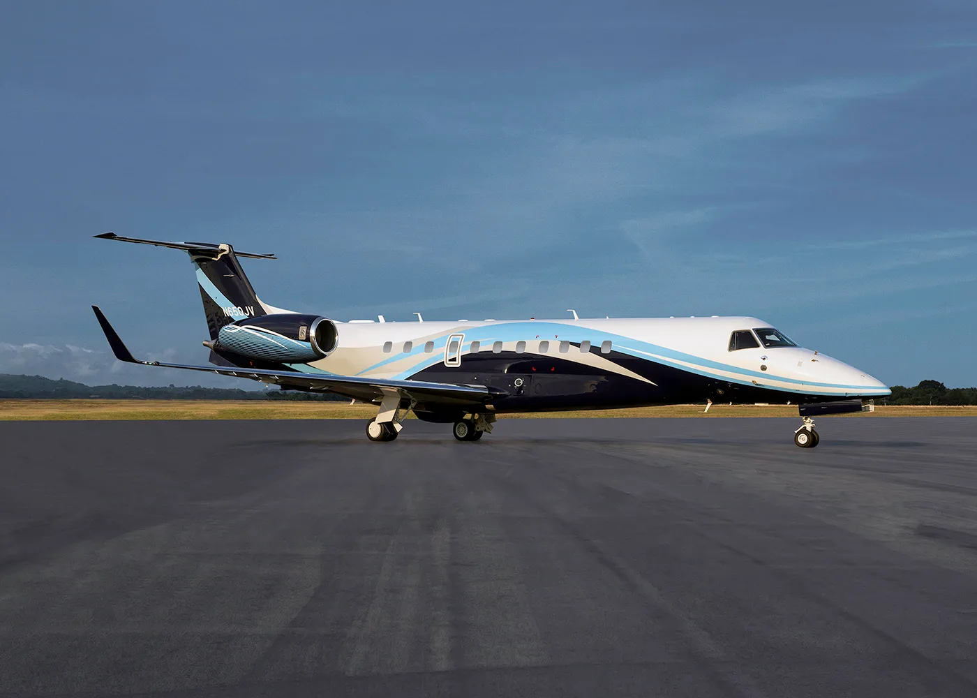 A white, black, and light blue Embraer Legacy business jet parked on an airfield under a blue sky.