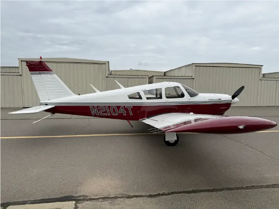 A white and maroon single-engine propeller aircraft, N2104T, is parked on an asphalt ramp with hangars in the background under a cloudy sky.