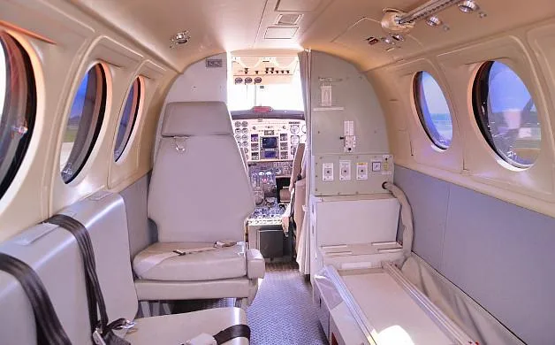 Another view of the aircraft's interior cabin, showing light gray seating, windows, and the cockpit entrance.