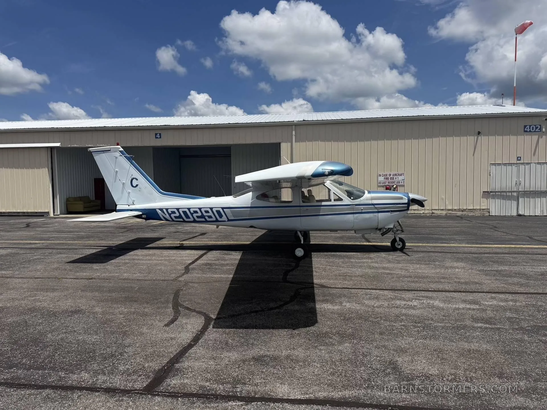 A side view of the white and blue Cessna aircraft, N20290, parked on a tarmac next to a hangar.