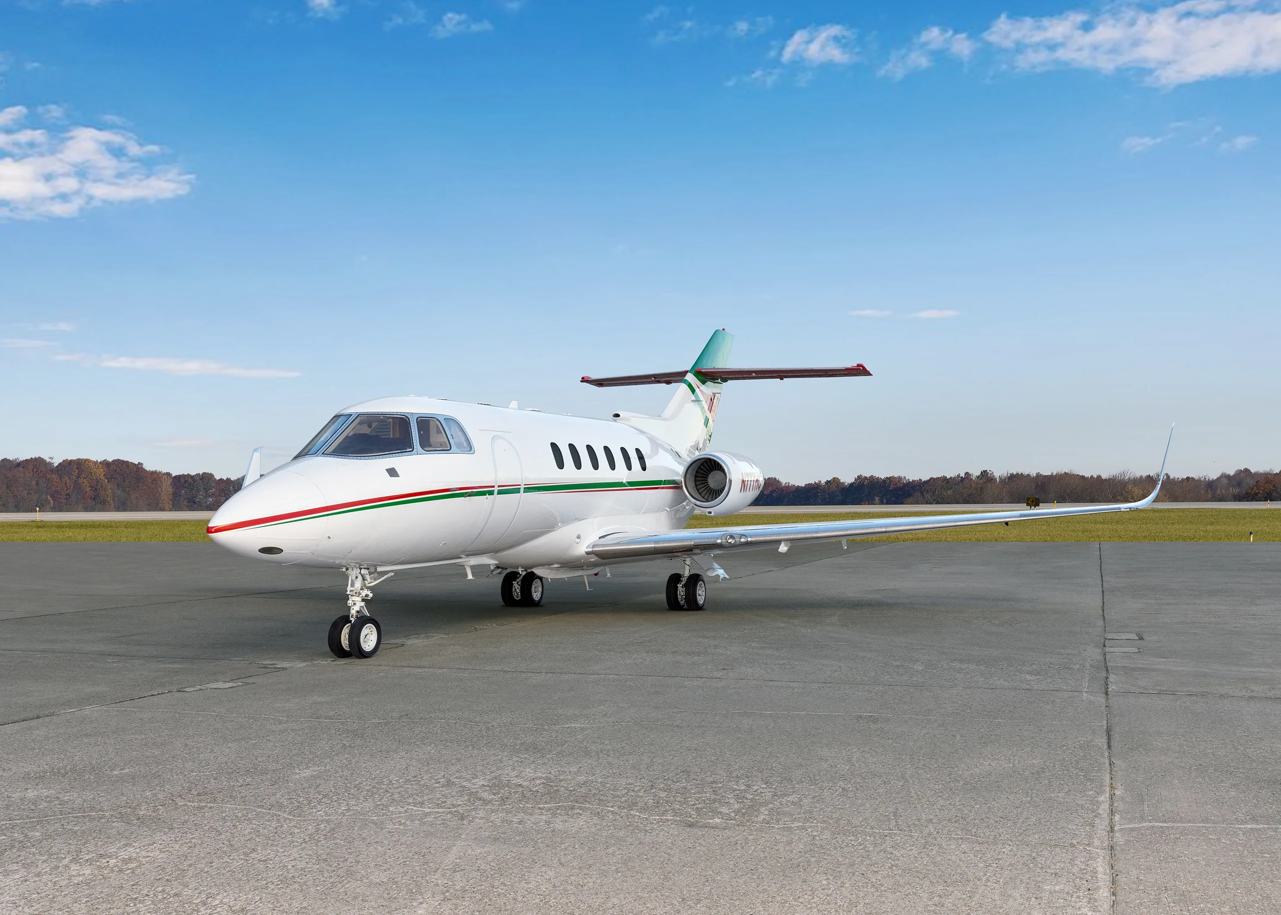 A white business jet with green and red stripes on the fuselage and tail, parked on an airfield.