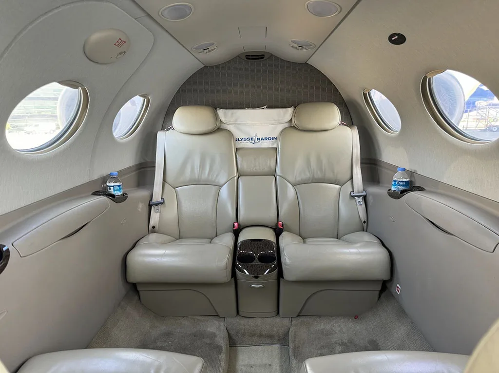 The aircraft's cabin interior showing two rows of light beige leather seats with a small console between the front two.