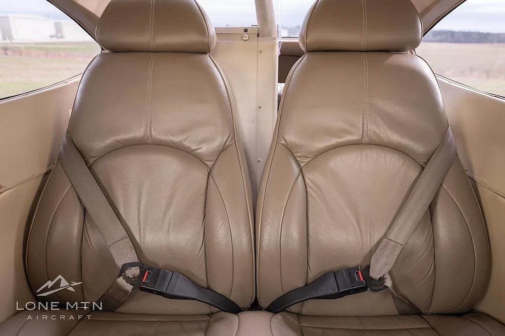 The tan leather rear seats of a Cessna 182 Skylane cabin, with seatbelts fastened, viewed from the front.