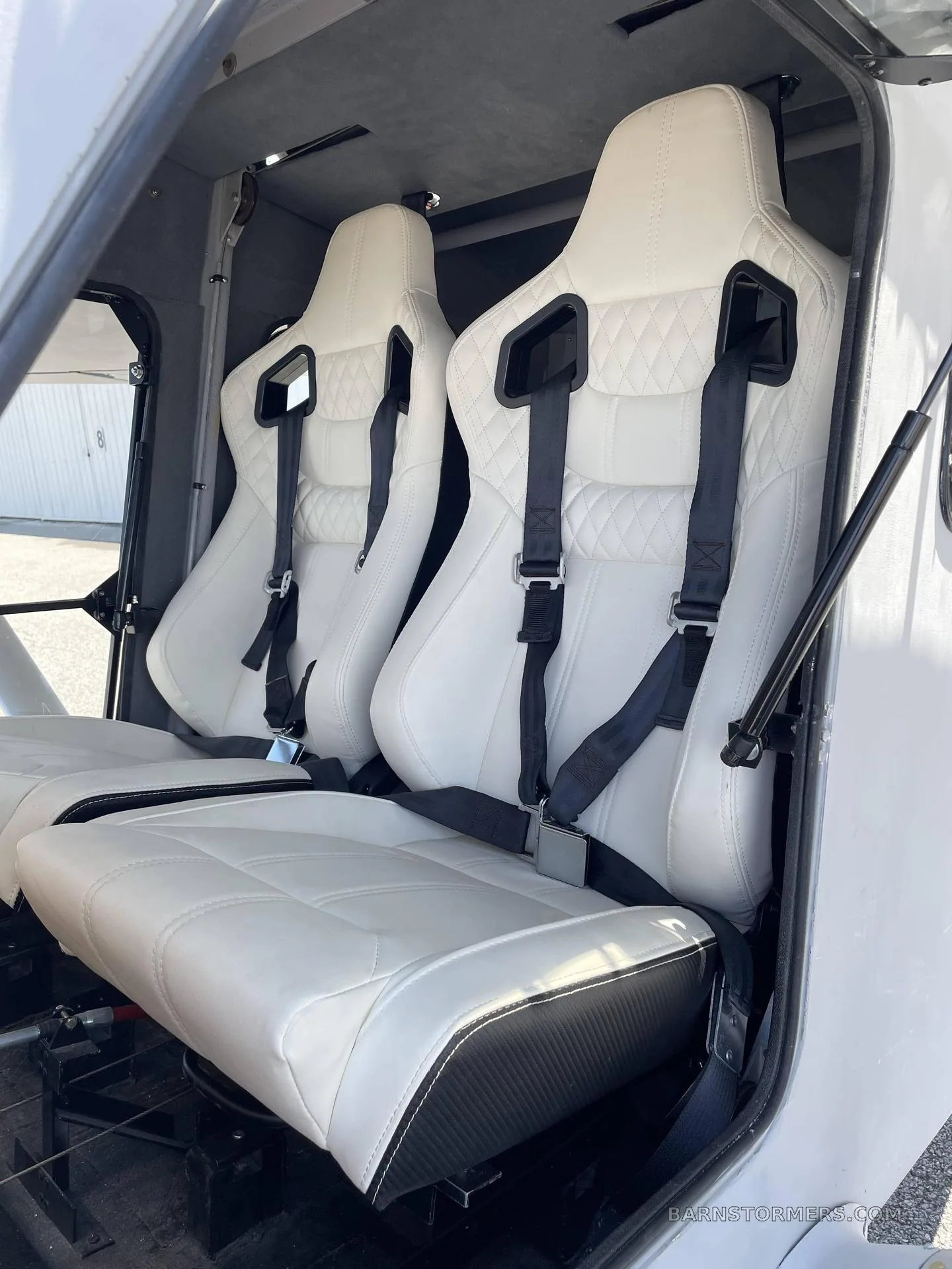 Two white quilted leather aircraft seats with black harnesses are visible inside the cabin.