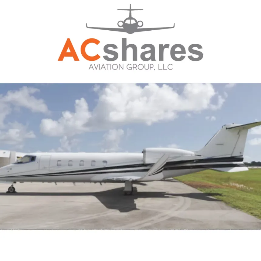 A white business jet with black stripes is parked on an airfield under a cloudy sky.