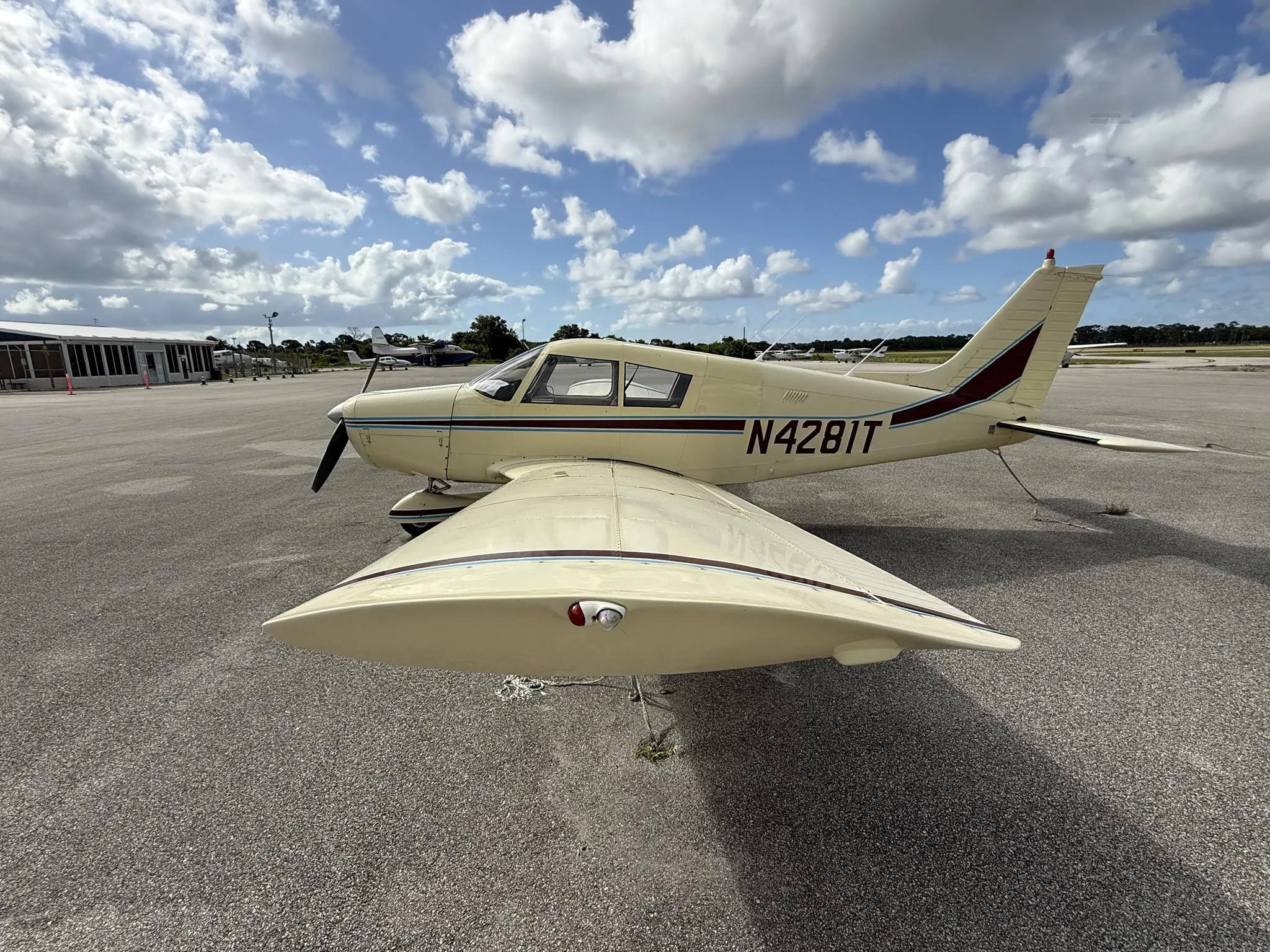 A cream-colored Piper PA-28-140E Cherokee, registration N4281T, parked on an airfield with its propeller visible.