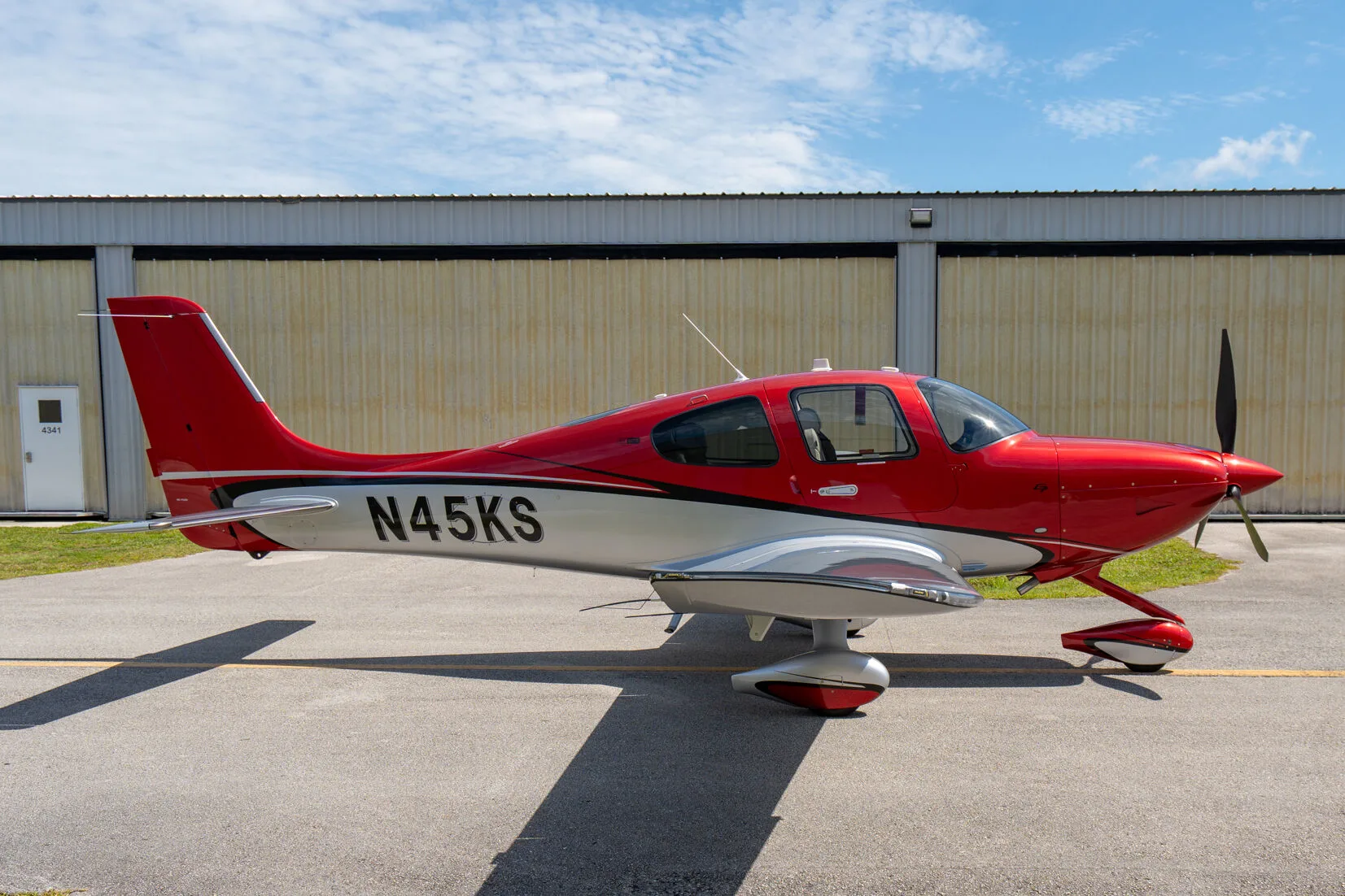 Side profile of a red and silver Cirrus SR22 GTS (N45KS) parked on an airfield.
