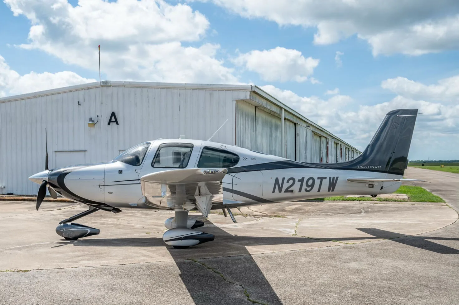 A side view of the Cirrus SR22T GTS Platinum aircraft N219TW with a white hangar in the background.