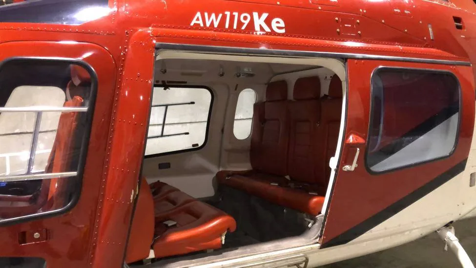 A close-up view of the open cabin door of a red and white AW119Ke helicopter, showing the brown leather seats inside.