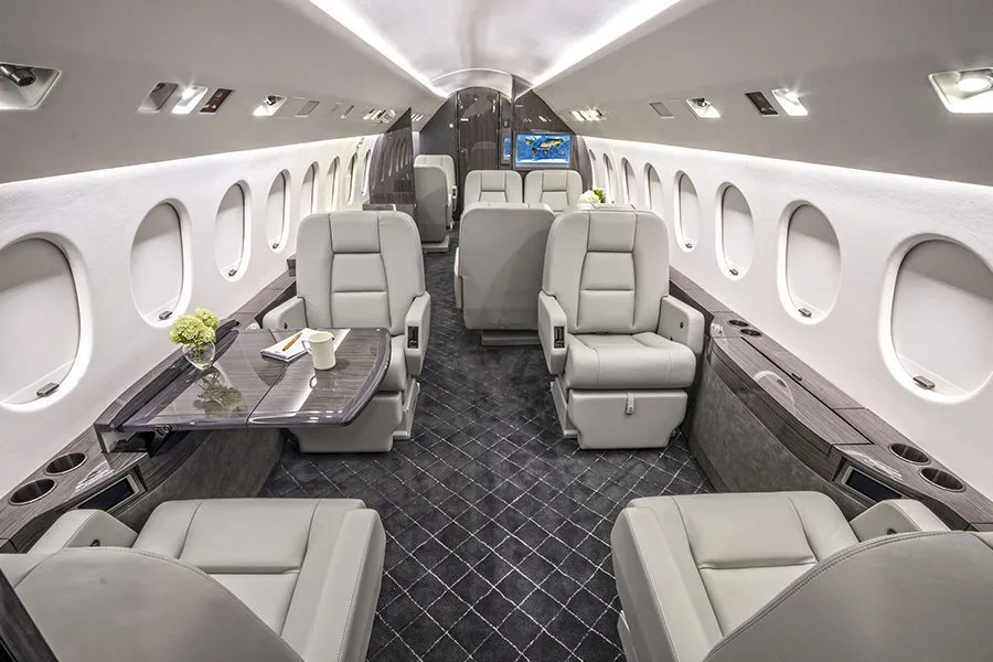 The luxurious cabin interior of a private jet with light grey leather seats and a dark patterned carpet.