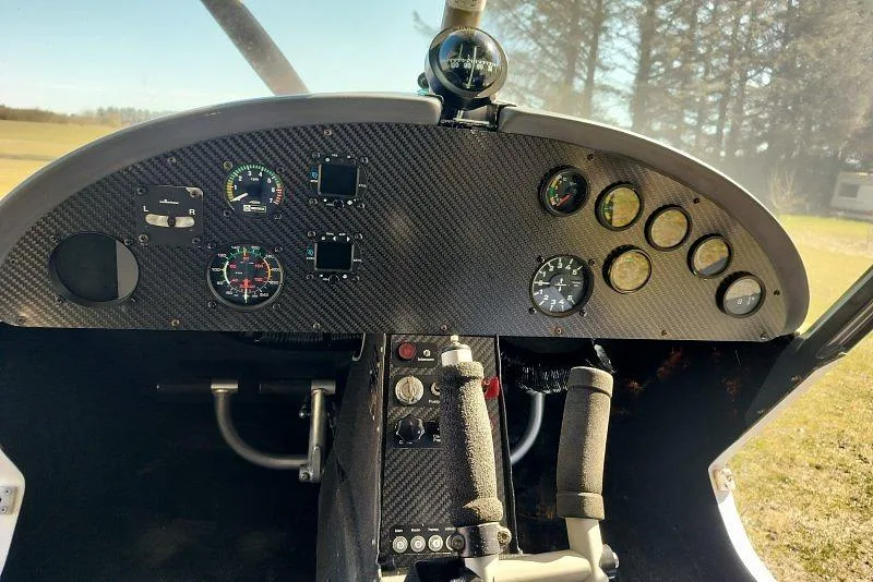 The cockpit of a light sport aircraft, featuring a carbon fiber instrument panel with various gauges and a central control stick.