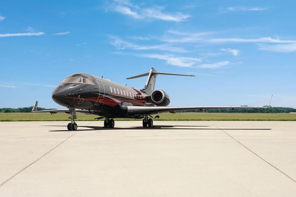A black and red Bombardier Global 7500 business jet is parked on a tarmac under a blue sky.