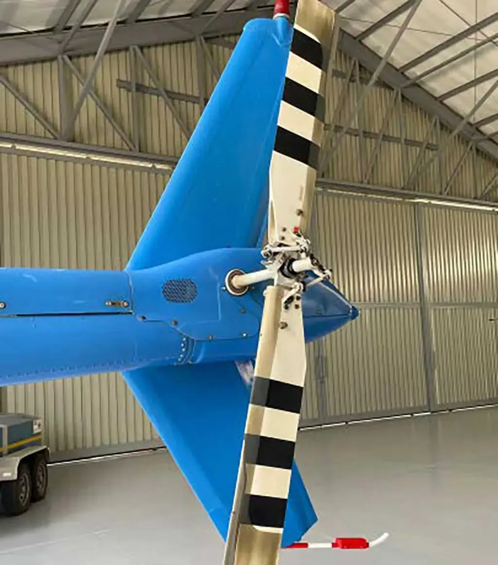 A close-up view of the blue tail boom and black and white striped tail rotor of a helicopter inside a hangar.