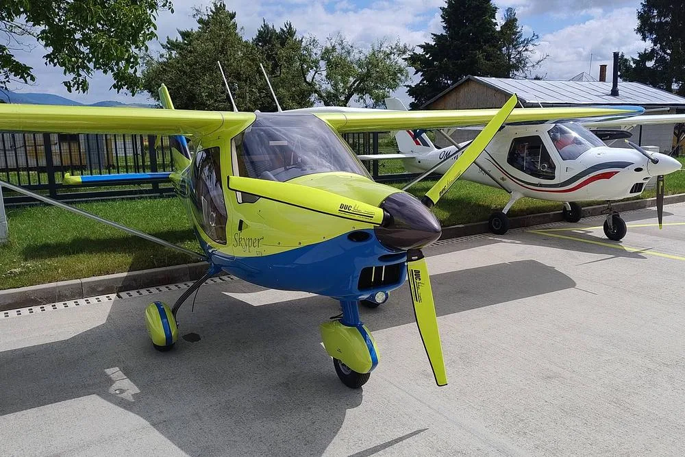 A yellow and blue Skyper GT9 aircraft parked on a tarmac next to another white aircraft.