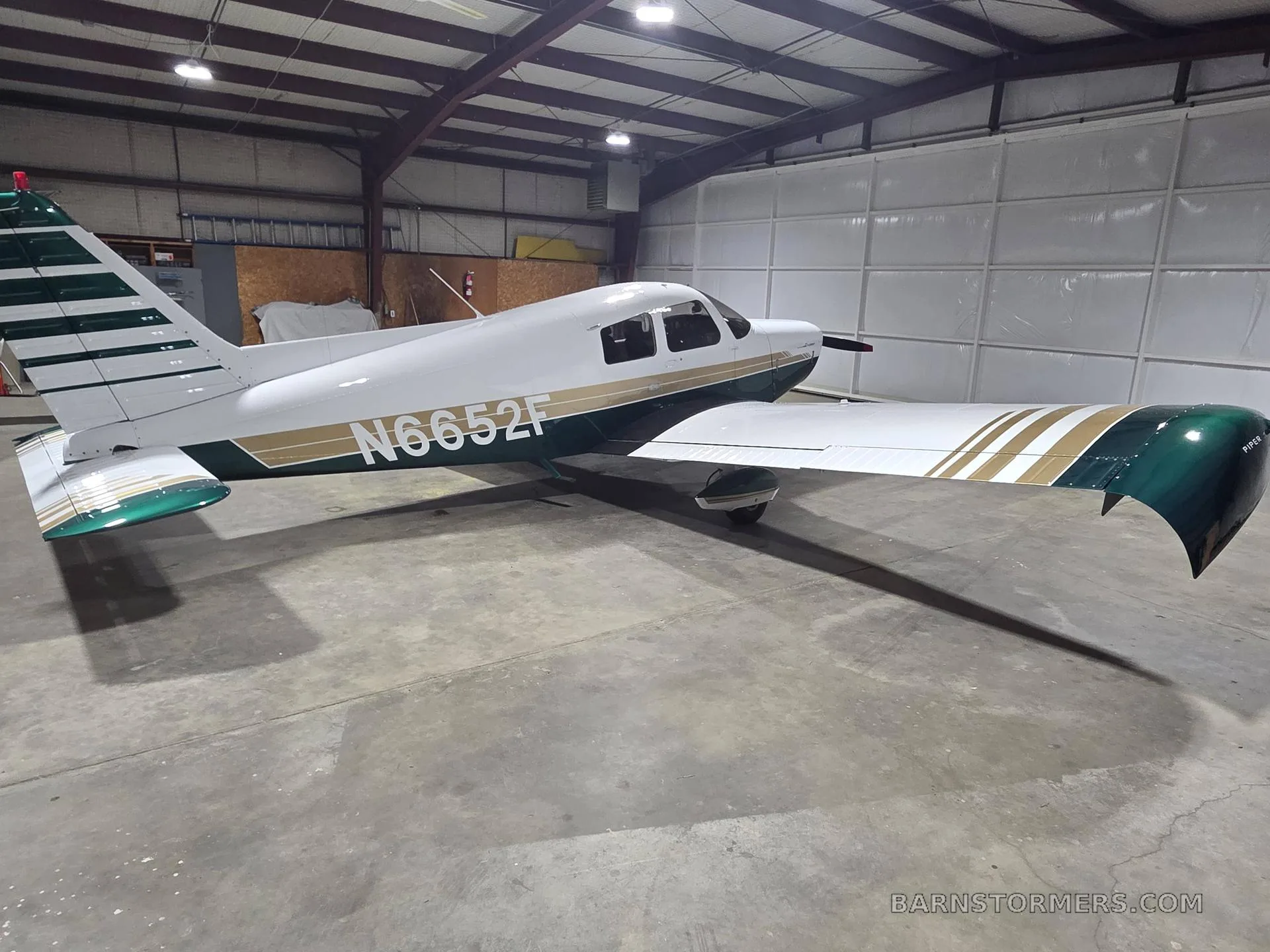A white and green single-engine propeller aircraft (N6652F) is parked inside a hangar, viewed from the rear left.