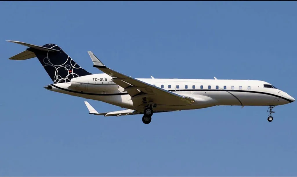 A white business jet with a black and white circular pattern on its tail is in flight against a clear blue sky.